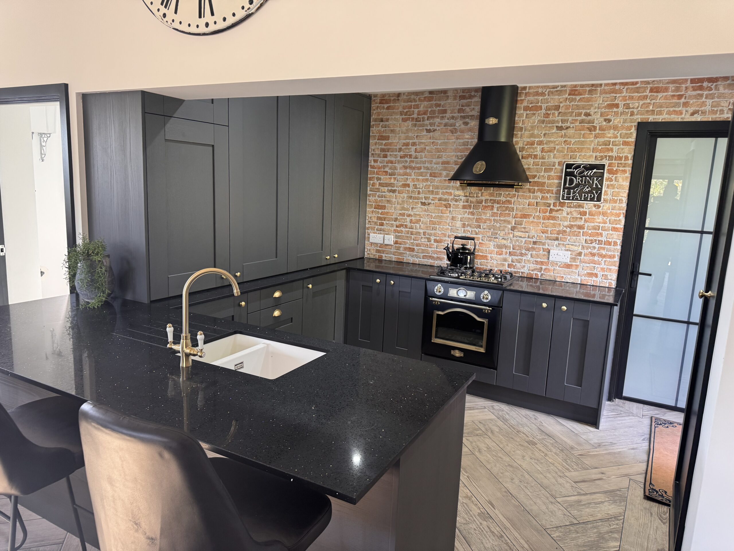 Dark Shaker kitchen with granite worktops, island seating and exposed brick feature wall